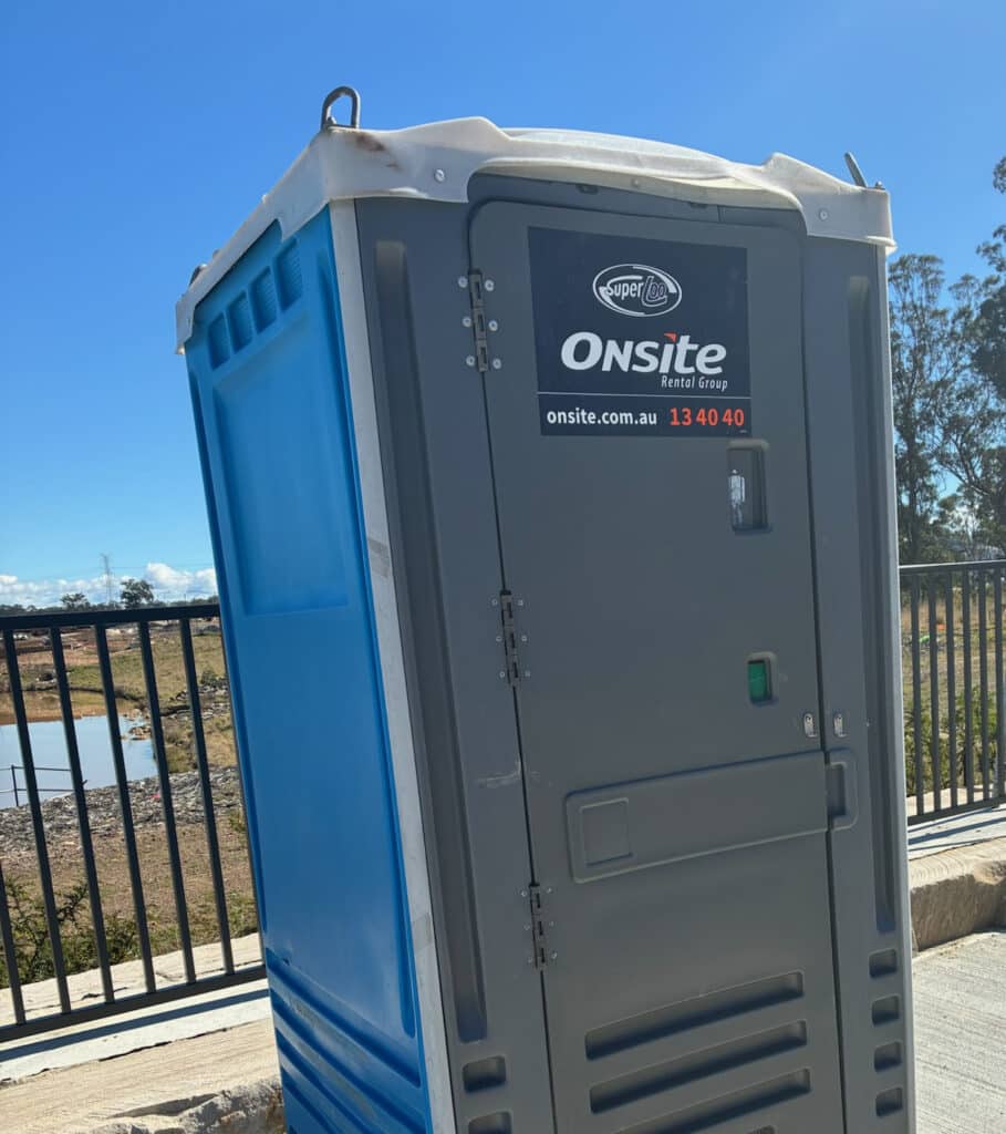 A mobile toilet cubicle being driven to site on a car trailer