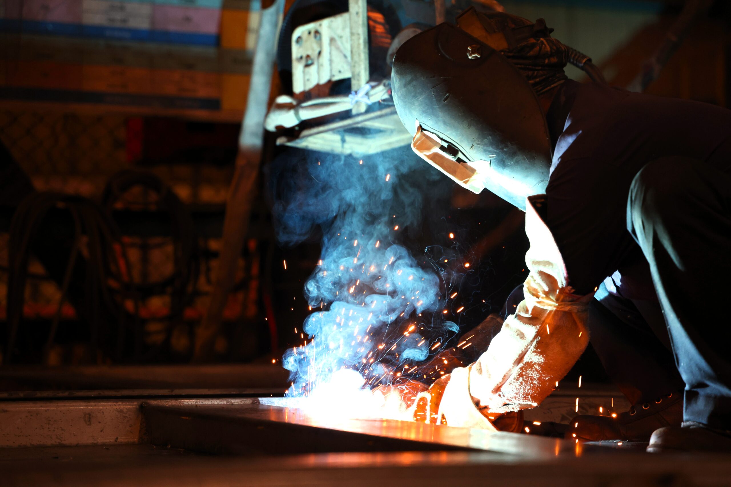 Welder in safety gear works on a metal structure as sparks fly.
