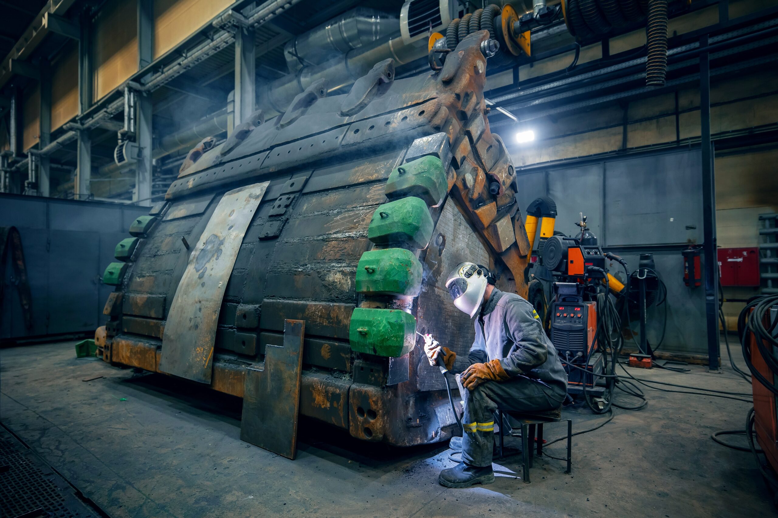 Welder in safety gear works on a metal structure as sparks fly.