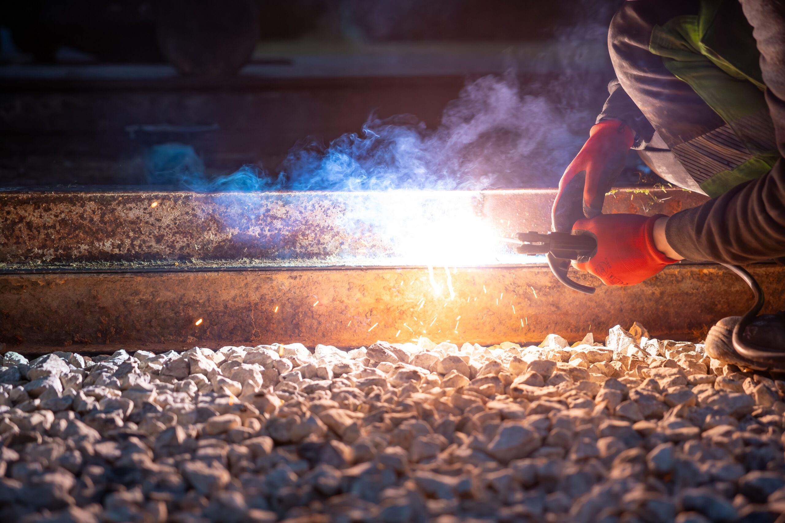 Welder in red gloves works on steel train tracks at night.